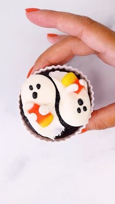 a person's hand holding a cupcake decorated with white frosting and black icing