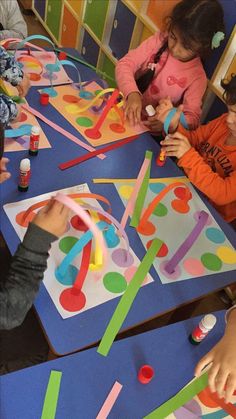 several children are sitting at a table making crafts with colored sticks and glues on paper