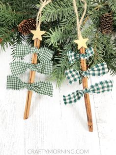 two wooden stick ornaments with green gingham bows and pine cones hanging from them