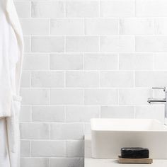 a white bathroom sink sitting next to a bath tub and shower curtain in front of a white brick wall