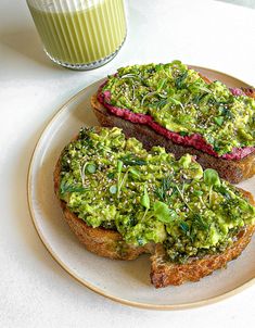 two pieces of bread with green toppings on them and a glass of milk in the background