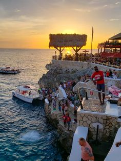 people are standing on the edge of a pier at sunset