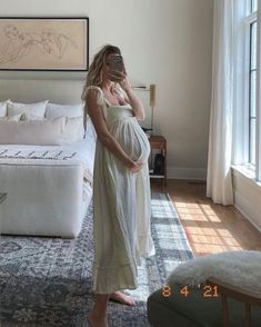 a pregnant woman takes a selfie in her bedroom while holding her baby bump up