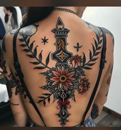 the back of a woman's tattoo with an ornate cross and flowers on it