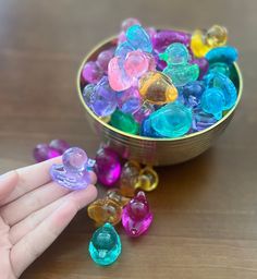 a hand is pointing at some colorful beads in a bowl