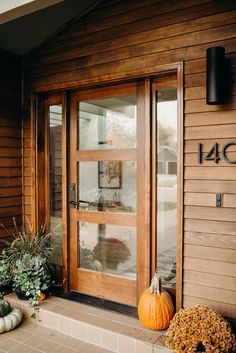 two pumpkins sitting on the front steps of a house with wooden siding and glass doors