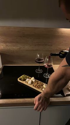 a man pouring wine into a glass on top of a kitchen counter with cheese and olives