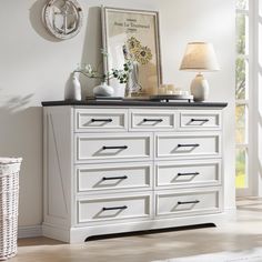 a white dresser with black top and drawers in a room next to a wall clock