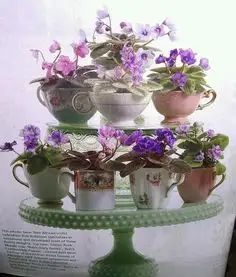 there are many cups that have flowers in them on the cake stand, and one has purple pansies growing out of it