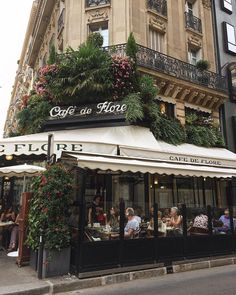 people sitting at tables in front of a cafe with plants growing on the building's roof