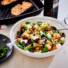 a white bowl filled with food next to a pan full of chicken and other foods