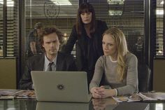 three people sitting at a table in front of a laptop computer with the screen turned on