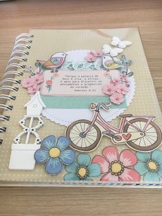 an open spiral notebook with flowers and a bicycle on the cover, sitting on a wooden table