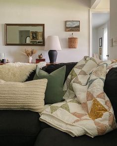 a living room filled with black couches covered in lots of pillows and throw blankets