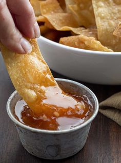 a person dipping some food into a small bowl with tortilla chips in it