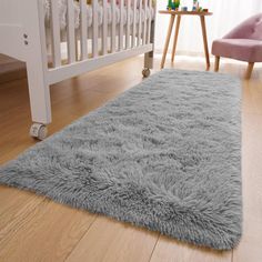 a baby's room with a white crib, pink chair and gray rug