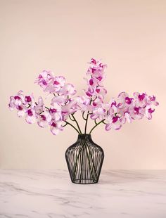 a black vase filled with purple flowers on top of a white marble counter topped with a pink wall