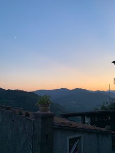 the sun is setting over some hills and mountains in the distance, with a bird perched on top of one of the buildings