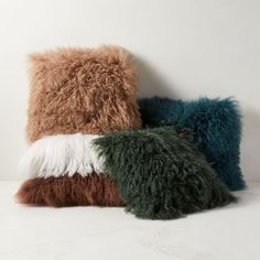 three different colored pillows sitting next to each other on a white surface, one is brown and the other is green