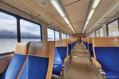 the inside of a train with blue seats and mountains in the backgrouds