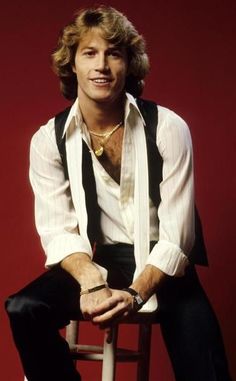 a man sitting on top of a wooden stool wearing a white shirt and black pants