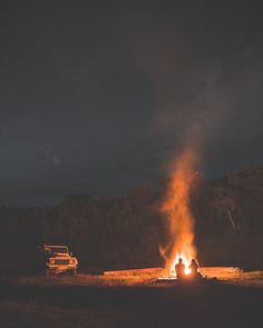 two people sitting around a campfire in the middle of a field at night time