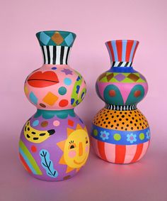 two colorful vases sitting next to each other on a pink surface with one painted in different colors