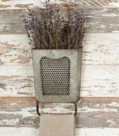 a metal planter with lavenders in it on a white wooden wall behind a towel holder