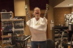 a woman holding up two guitars in front of a recording room full of sound equipment