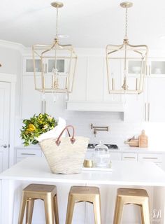 a white kitchen with gold bar stools and hanging lights over the island countertop