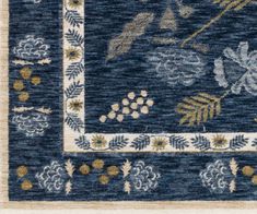 a blue rug with gold and white designs on the border, including leaves and flowers