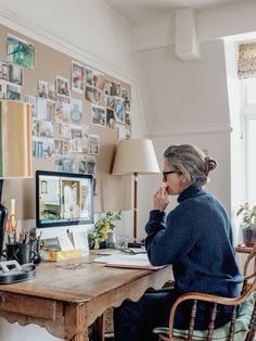 an older woman sitting at a desk in front of a computer monitor and keyboard, working on her laptop