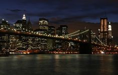 the city skyline is lit up at night as seen from across the water in new york