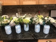 four blue vases with white flowers in them on a kitchen counter next to a stove