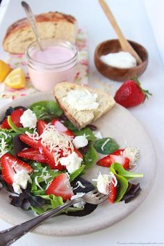 a white plate topped with a salad covered in cheese and strawberries next to a bowl of yogurt