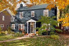 a large blue house surrounded by trees and leaves in the fall with autumn foliage on the ground