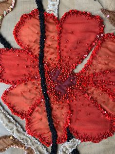 a red flower with sequins on it sitting on top of a piece of cloth