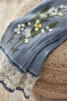 a pair of jeans with flowers on them sitting on top of a rug next to a straw hat