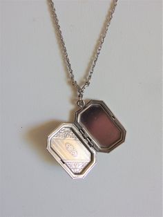 "Lovely vintage Art Deco style locket pendant from designer 1928. The locket measures 1 1/8\" long x 3/4\" wide and is hung on a 26\" long silver tone chain. The locket has pretty etching on the front and an oval blue glass cabochon. It is in very good condition and is marked \"1928\" on a tag. Please email me with any questions and thanks for looking!" Antique Silver Medallion Locket Necklace With Vintage Charm, Classic Pendant Locket Necklace, Vintage Antique Silver Locket Necklace, Classic Vintage Charm Locket Necklace Collectible, Antique Silver Sterling Silver Vintage Locket Necklace, Vintage Silver Necklaces For Memorial, Vintage Engraved Rectangular Pendant Necklace, Antique Silver Vintage Charm Pendant Locket Necklace, Vintage Locket Necklace With Rectangular Pendant