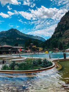 people are swimming in an outdoor pool with mountains in the background and blue skies above