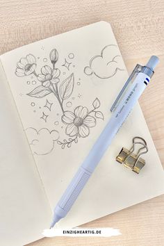 an open notebook with a pen and flower drawing on it next to a pair of scissors