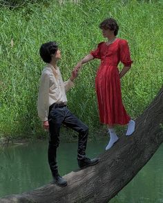 a man and woman standing on a tree branch in front of a body of water