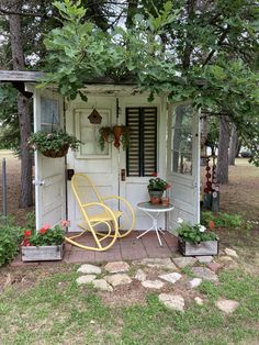 a small white shed with a yellow rocking chair and potted plants on the porch