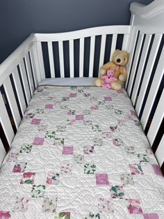 a teddy bear sitting on top of a crib with a quilt in it's bed