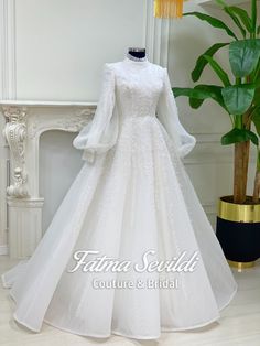 a white wedding dress with long sleeves on display in front of a potted plant