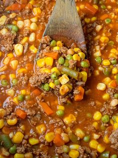 a wooden spoon is full of soup with corn and carrots on the side,