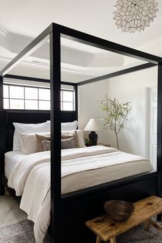 a bedroom with a four poster bed and white sheets on the bed, along with a wooden footstool