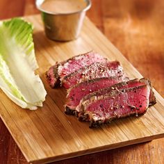 sliced meat and lettuce on a cutting board with a cup of dipping sauce