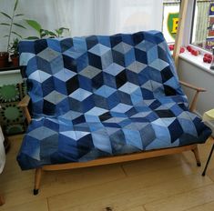 a couch covered in a blue and black quilt next to a window with potted plants