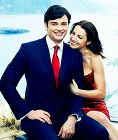 a man in a suit and tie sitting on a bench next to a woman wearing a red dress